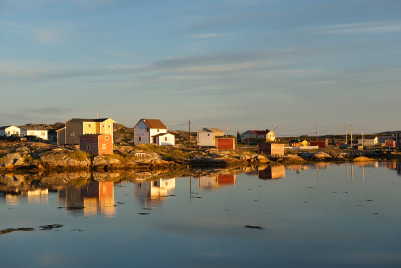 Colorful houses on rocky coast reflect in calm water at sunset