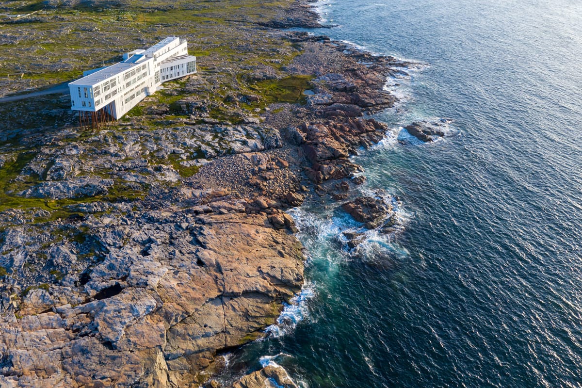 Modern coastal architecture, Fogo Island Inn building on stilts, rocky shoreline, ocean, green moss, aerial view of rugged coast