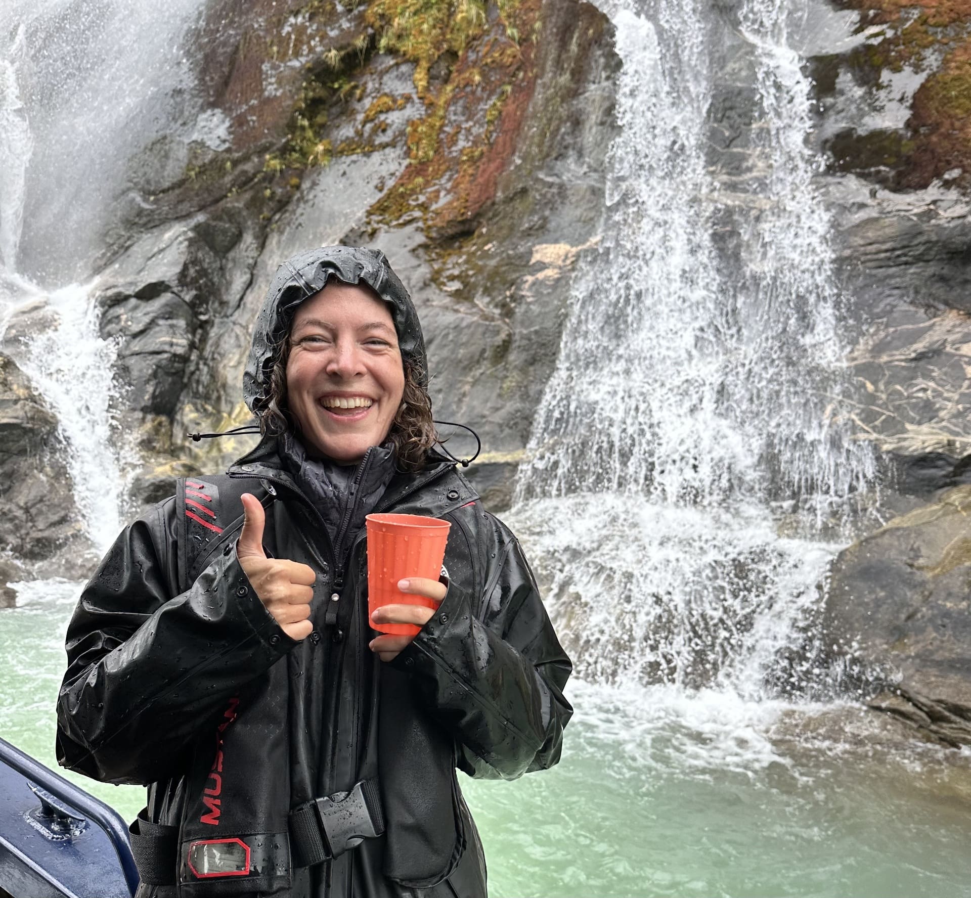 A passenger enjoys a drink of glacier water from a waterfall