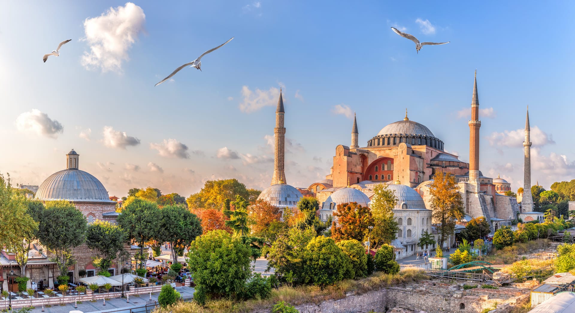Hagia Sophia Grand Mosque Courtesy of Turkiye Tourism Promotion & Development Agency Hagia Sophia in Istanbul with domes, minarets, flying seagulls, and autumn trees under a blue sky