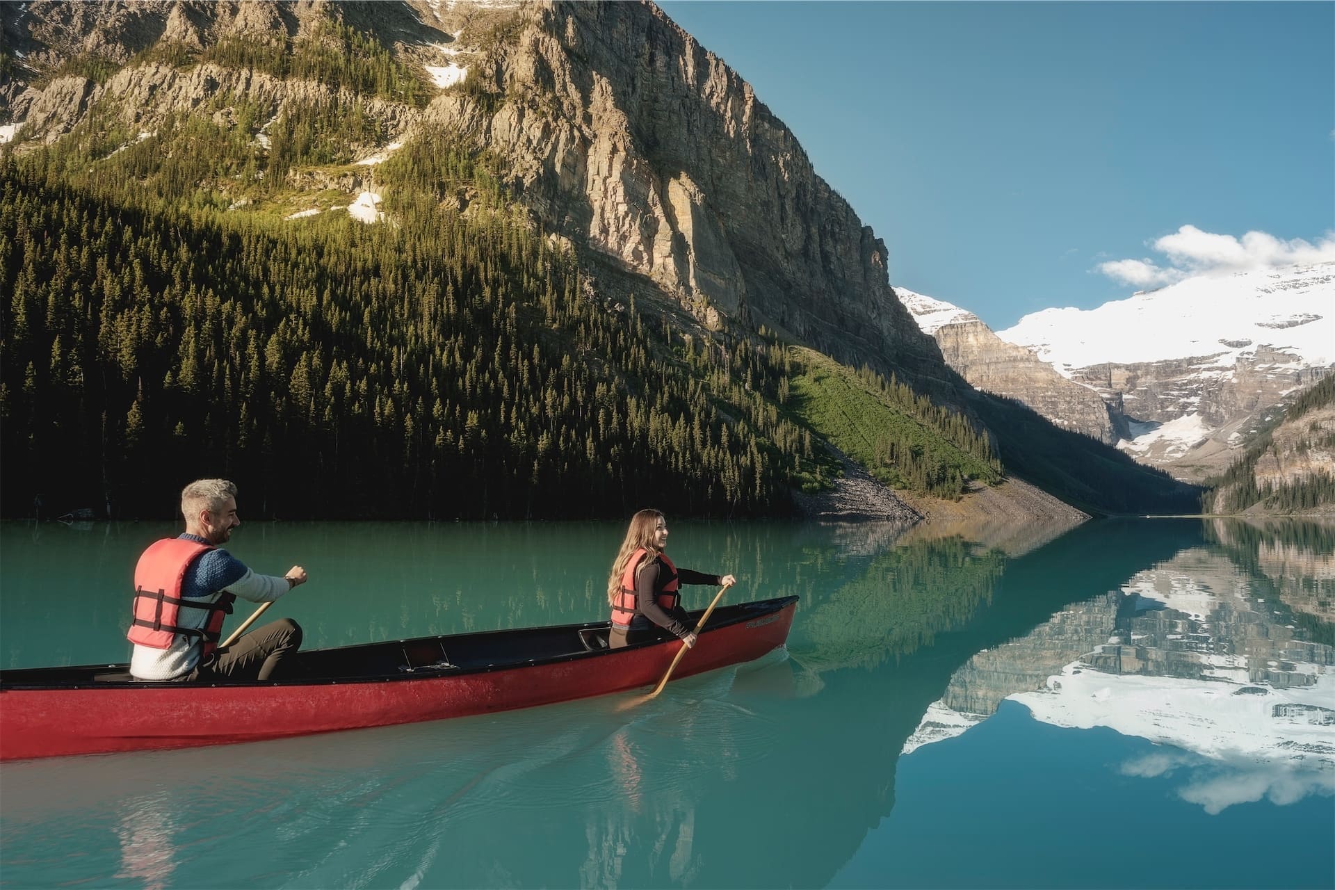 Paddlers take one of the signature red rental canoes on Lake Louise, with Mt. Victoria in the foreground